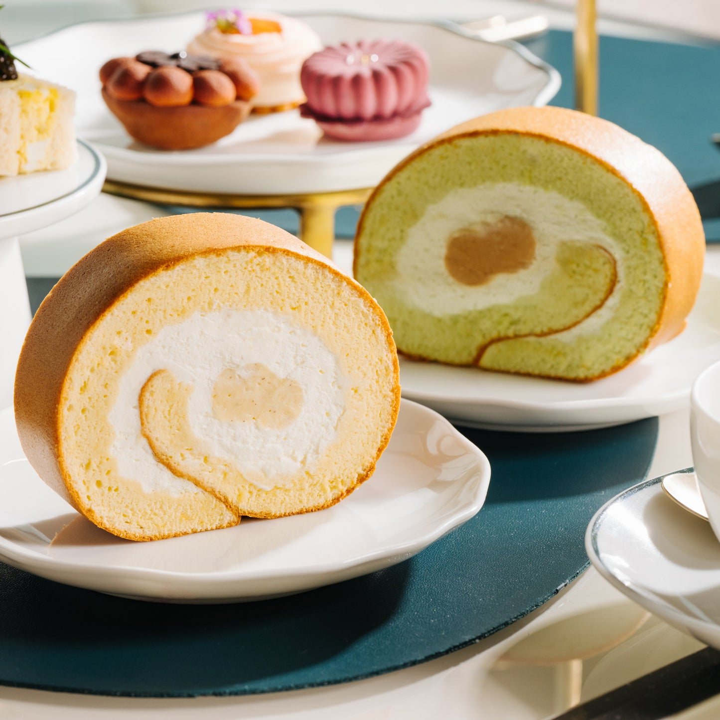 Two Regent roll cakes on a table with tea cups and other pastries.